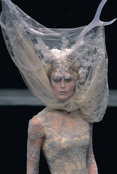 a woman wearing a veil and dress with flowers on it's head is walking down the runway