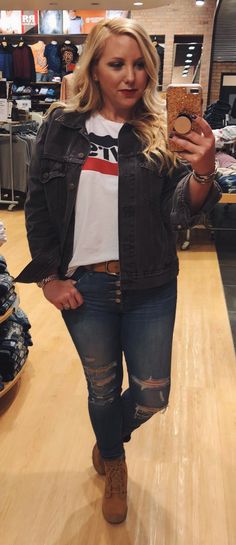 a woman taking a selfie with her cell phone in a clothing store while wearing ripped jeans and a denim jacket