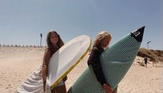 two women are holding surfboards on the beach