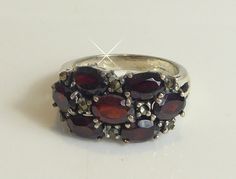 A fine solid silver band ring set with seven oval cut real garnets interspersed with marcasite stones. the garnets have a lovely deep blood red colour. the front of the ring measures 1cm high tapering down to 2mm at back on silver band. ring size uk-m. stamped omn inside ring. looks stunning when worn.in very good condition.