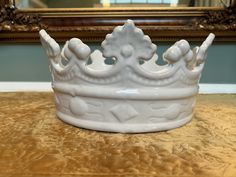 a white ceramic crown sitting on top of a table next to a framed mirror in a room