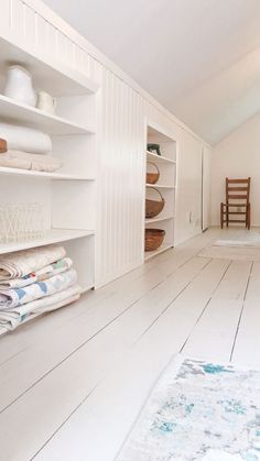 a room with white walls and flooring has shelves on each side, two chairs in the middle