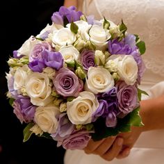 a bride holding a bouquet of white and purple flowers