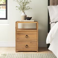 a nightstand with two drawers and a potted plant sitting on top of it next to a bed