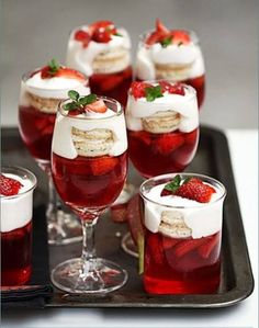 there are many desserts and drinks on the tray with strawberries in glasses next to each other