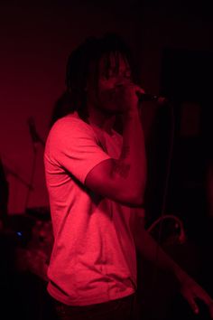 a man with dreadlocks singing into a microphone in front of a red light