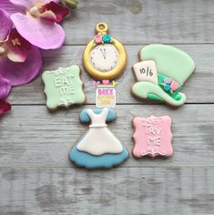 some decorated cookies are sitting on a wooden table next to purple flowers and a clock