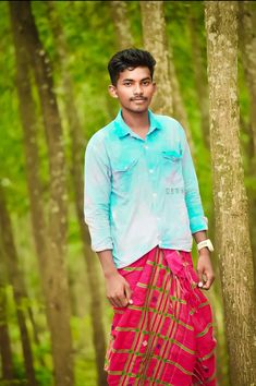 a man standing next to a tree in a forest wearing a blue shirt and red pants