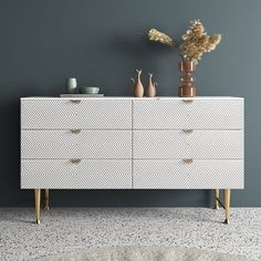 a white dresser with two vases on top and a plant in the corner next to it