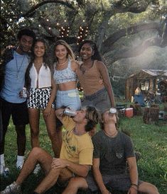 a group of young people sitting on the ground in front of a tree with string lights