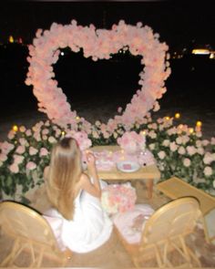 a woman sitting at a table with flowers in the shape of a heart on it