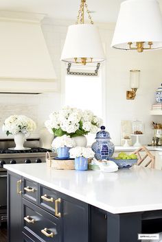 a kitchen with two lamps hanging from the ceiling and white flowers in vases on the counter