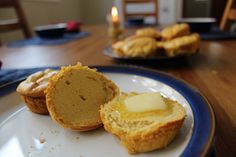 two muffins on a plate with butter and some other pastries in the background