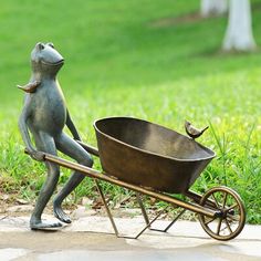 a statue of a frog pushing a wheelbarrow with a bird perched on it