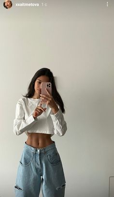 a woman taking a selfie while wearing ripped jeans and a cropped white top