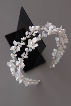 a close up of a tiara on a black stand with white flowers and pearls