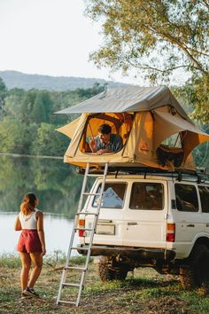 a man and woman standing in front of a van with a tent on top