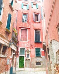 an alley way with red brick buildings and green shutters on the windows, in venice