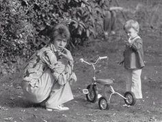 an old black and white photo of two children playing with a tricycle in the yard