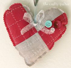 a red heart shaped ornament with a sewing needle in the middle and a button on it