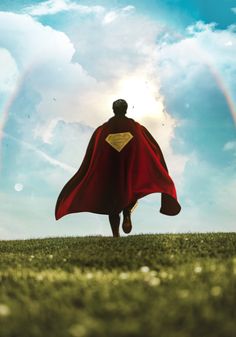 a man in a red cape is running through the grass with a rainbow behind him