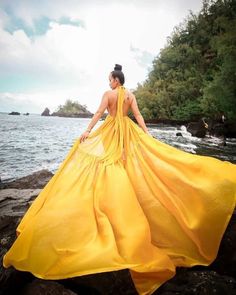 a woman in a yellow dress standing on rocks by the water