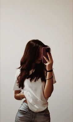 a woman taking a selfie with her cell phone in front of her face and wearing a white t - shirt