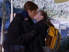 a man and woman kissing each other in front of trees with snow on the ground