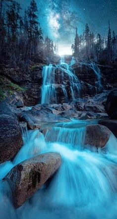 a waterfall with blue water flowing down it's side under a night sky filled with stars