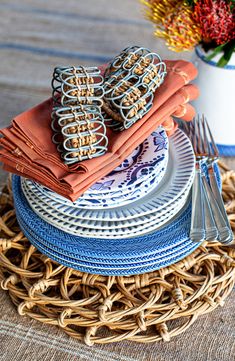 a stack of plates with napkins and forks on top of each other next to a flower vase