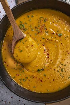 a wooden spoon in a pot filled with yellow soup and garnished with parsley