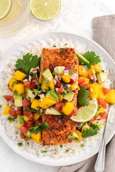 a white plate topped with fish and rice covered in mango salsa next to lime wedges