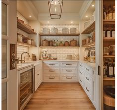 an open kitchen with white cabinets and wooden flooring, along with shelves filled with wine bottles