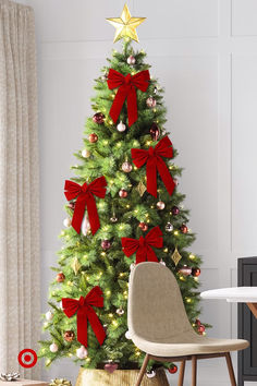 a decorated christmas tree with red bows and gold ornaments in a living room area, next to a chair