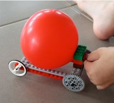 a person is holding a red balloon on a small toy cart with wheels and gears