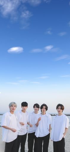 group of young men standing next to each other on top of a sandy beach under a blue sky