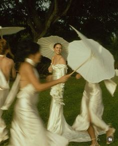 two women in white dresses are holding umbrellas while another woman is walking behind them