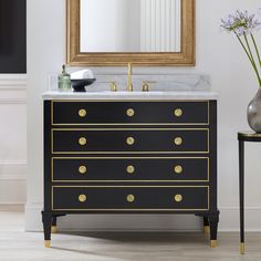 a black and gold bathroom vanity with marble counter top, brass knobs on the drawers