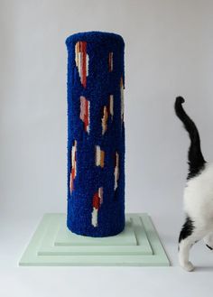 a black and white cat standing next to a tall blue object with red, white, and blue designs on it