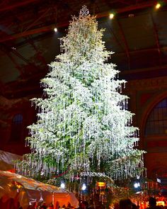 a large christmas tree is lit up in the middle of a room filled with people