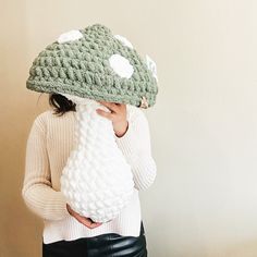 a woman wearing a crocheted hat covering her face with a knitted object