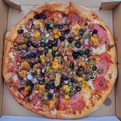 a pizza in a box with toppings and meat, cheese, olives, pepperoni, peppers, onions, sausage, and more