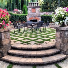 an outdoor patio with stone steps leading to a fire place and dining table surrounded by flowers