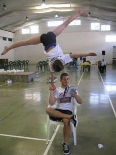 two men are doing tricks on chairs in an indoor gym while one man is upside down