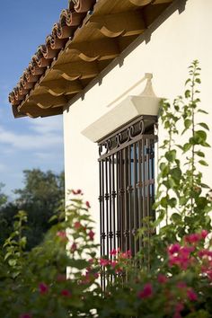 an iron window on the side of a white building with pink flowers in front of it