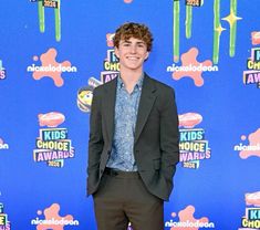 a young man in a suit and tie standing on the red carpet at an awards event