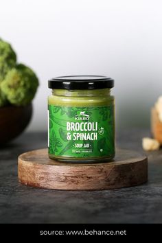 a jar of broccoli and spinach spread on a cutting board next to some broccoli