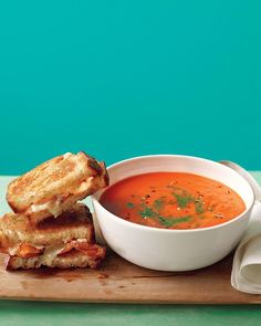 a bowl of soup and grilled cheese sandwich on a cutting board