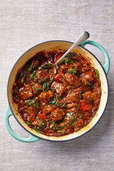 a pot filled with meat and vegetables sitting on top of a table next to a spoon