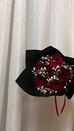 a bouquet of red roses in a black paper hat with baby's breath and baby's breath